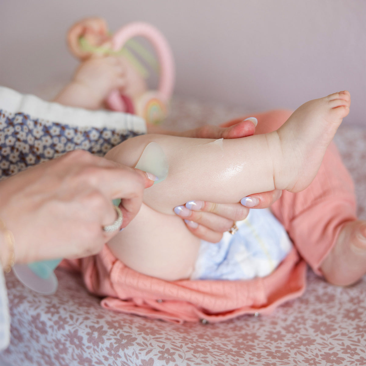 A caretaker using the green Olababy silicone spatula to gently apply diaper rash ointment to a baby's leg, keeping fingers completely clean.