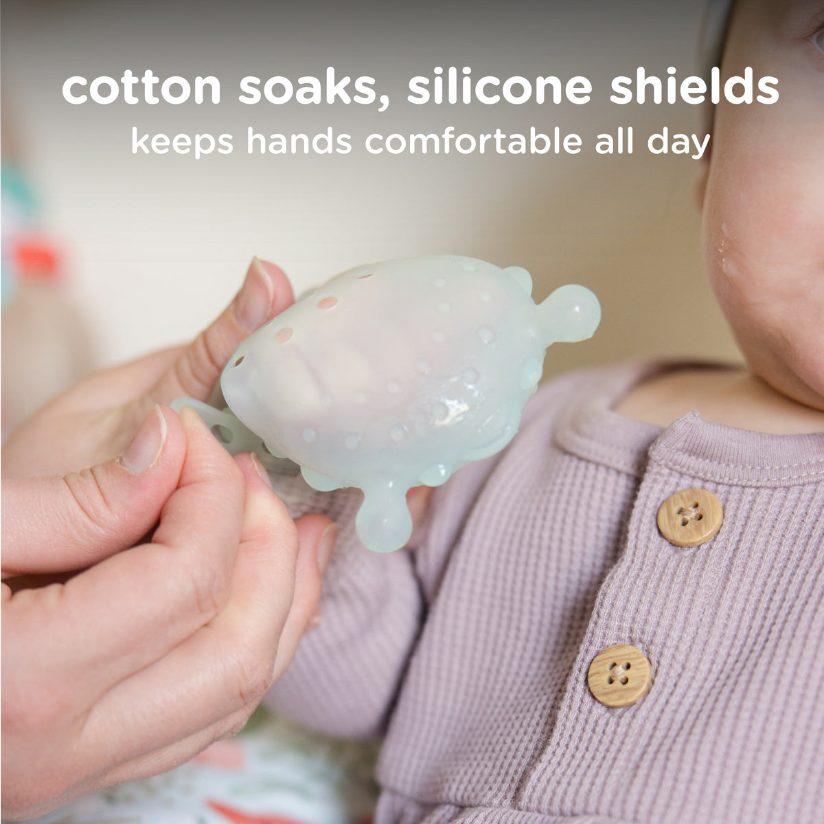 A side-by-side photo comparison of a baby's hand: one wearing a standard cotton mitten marked as "cotton soaks" and "soggy", and the other wearing a lavender Olababy silicone mitten marked as "silicone shields" and "dry".
