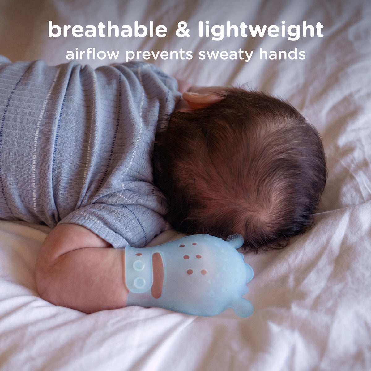 A baby lying on white bedding wearing a light blue silicone teething glove on one hand, with text at the top reading 'breathable & lightweight' and 'airflow prevents sweaty hands'.